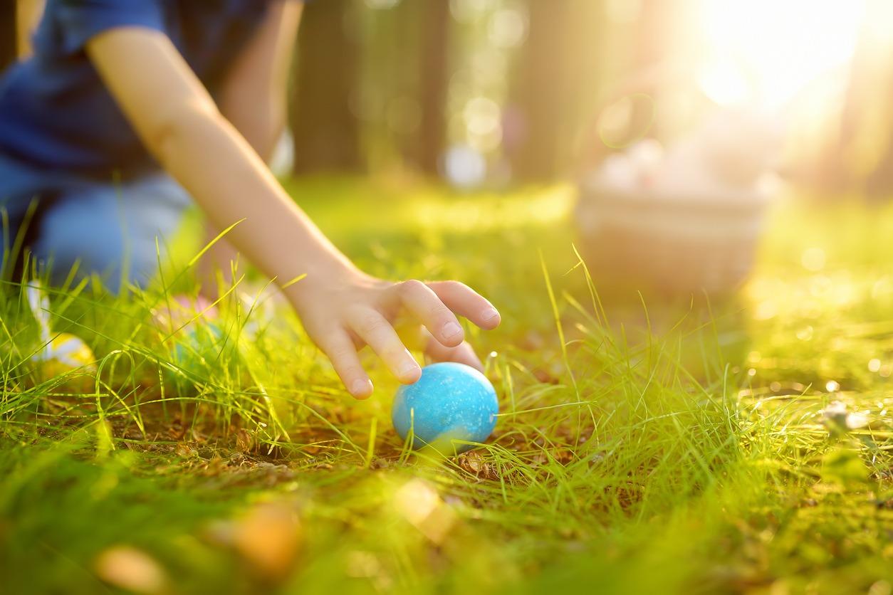 young boy picking up an egg in the grass at an egg hunt.