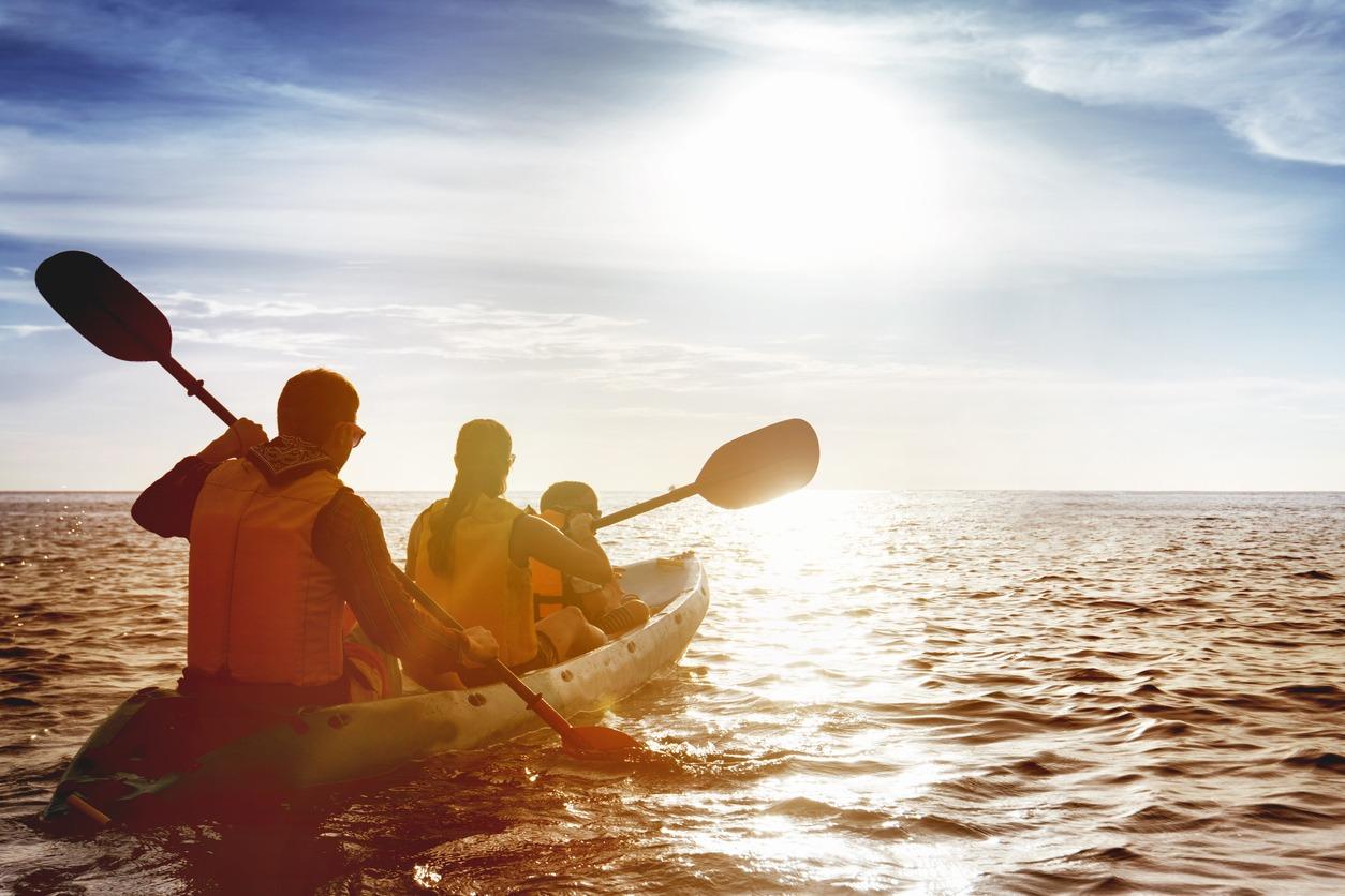 Family out kayaking on open water while at the beach during evening hours.